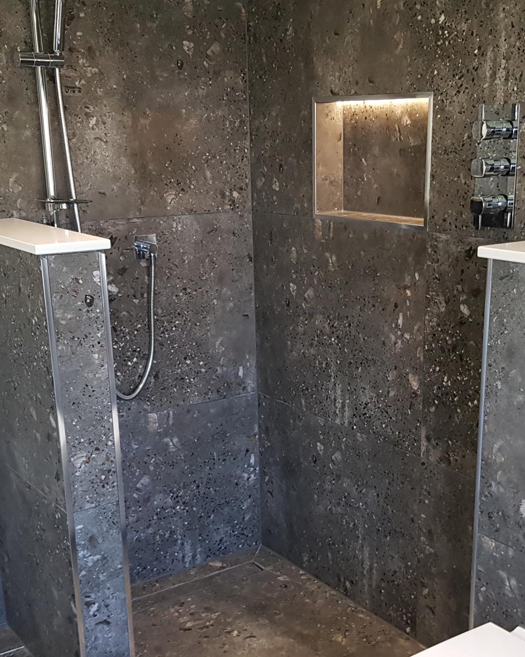 Walk-in shower in charcoal terrazzo-effect tiles with a lit wall niche and chrome shower valves