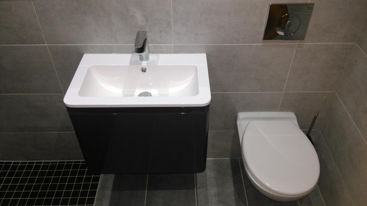 Gloss black wall-hung vanity unit beside a wall-hung WC, with black mosaic shower floor tiles