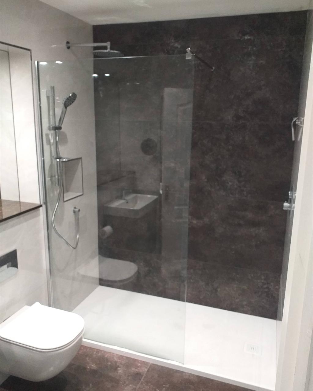 Walk-in shower with a frameless glass screen against a dark marble-effect wall